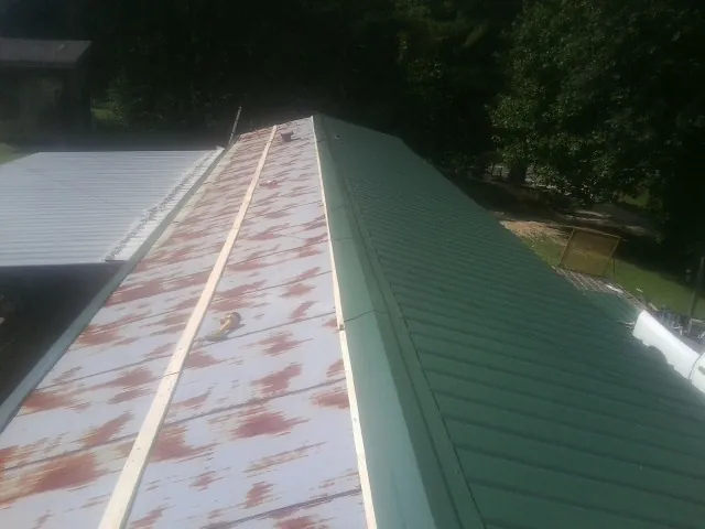 Old rusted panels beside newly installed green metal roofing — Wind Damage Roof Repair by Roofing Brothers in Watertown