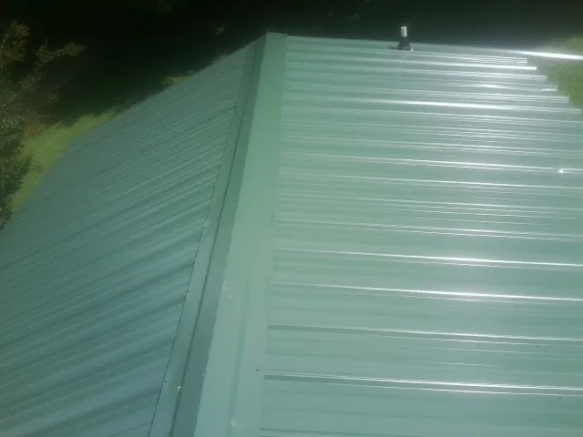 New green metal panels meeting at the ridge of a roof — Flat Roof Repair work by our crew in Watertown