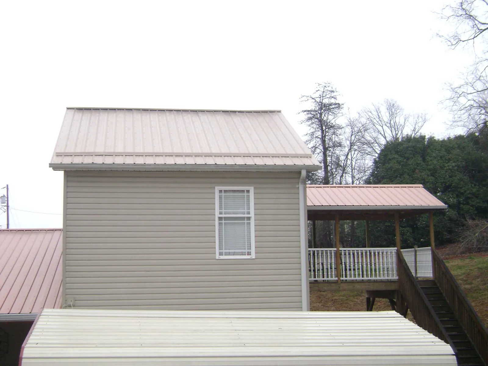 Tan metal roofs on a two story addition and attached porch, from a Roof Replacement job in Watertown